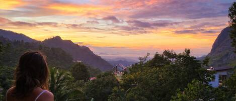 A woman overlooking a mountainous landscape with a sunset.