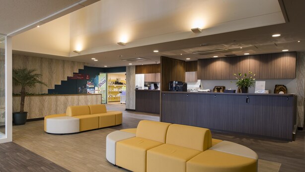 A modern reception area with a curved yellow sofa, a reception desk, and a staircase leading to an upper level.