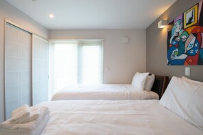 A hotel room with two beds, a large window with blinds, a painting on the wall, and a set of towels on the bed. - Holiday Niseko Flow Niseko (Kutchan)