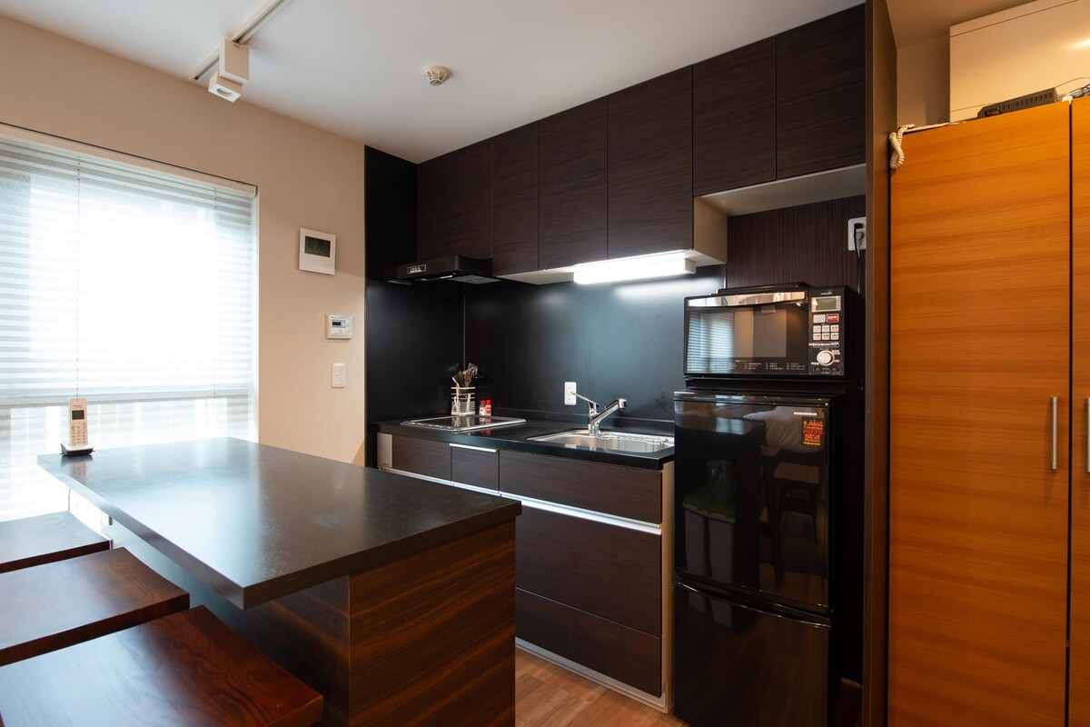 A modern kitchen with dark cabinetry, a stainless steel refrigerator, and a built-in oven.