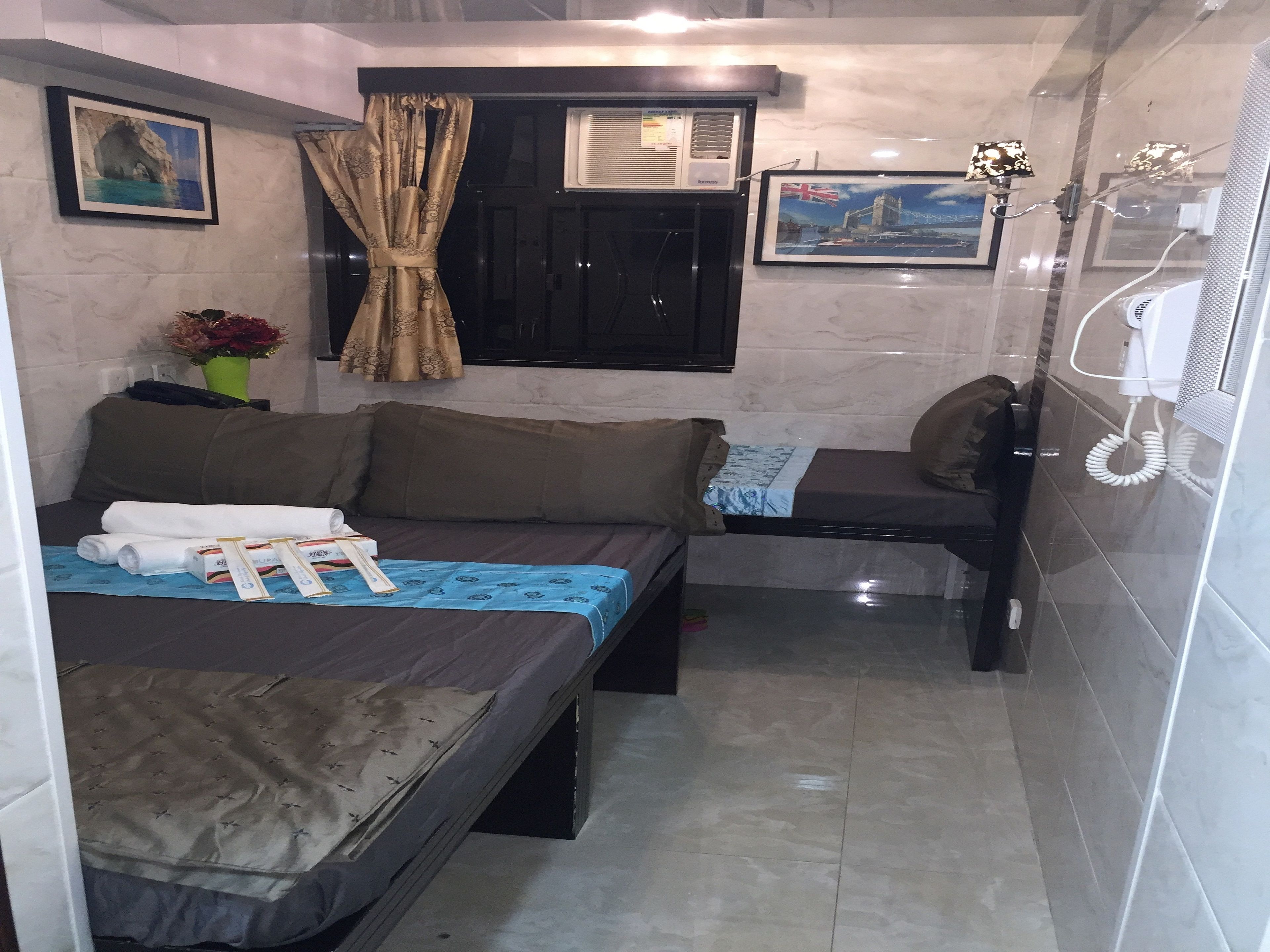 Habitación pequeña con cama, un sofá compacto, ventana con cortinas, aire acondicionado instalado en la pared y un cuadro enmarcado.