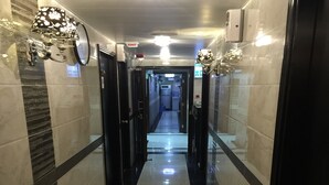 A corridor with reflective black and white tiled floors, wall-mounted lamps, and a door at the end. - Hi-Inn (Kowloon)