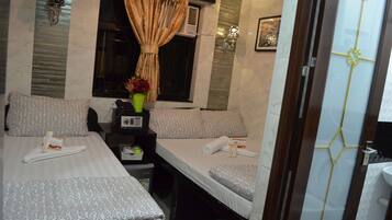 A hotel room with two beds, a small desk with a telephone, a vase with flowers, and a window with curtains.