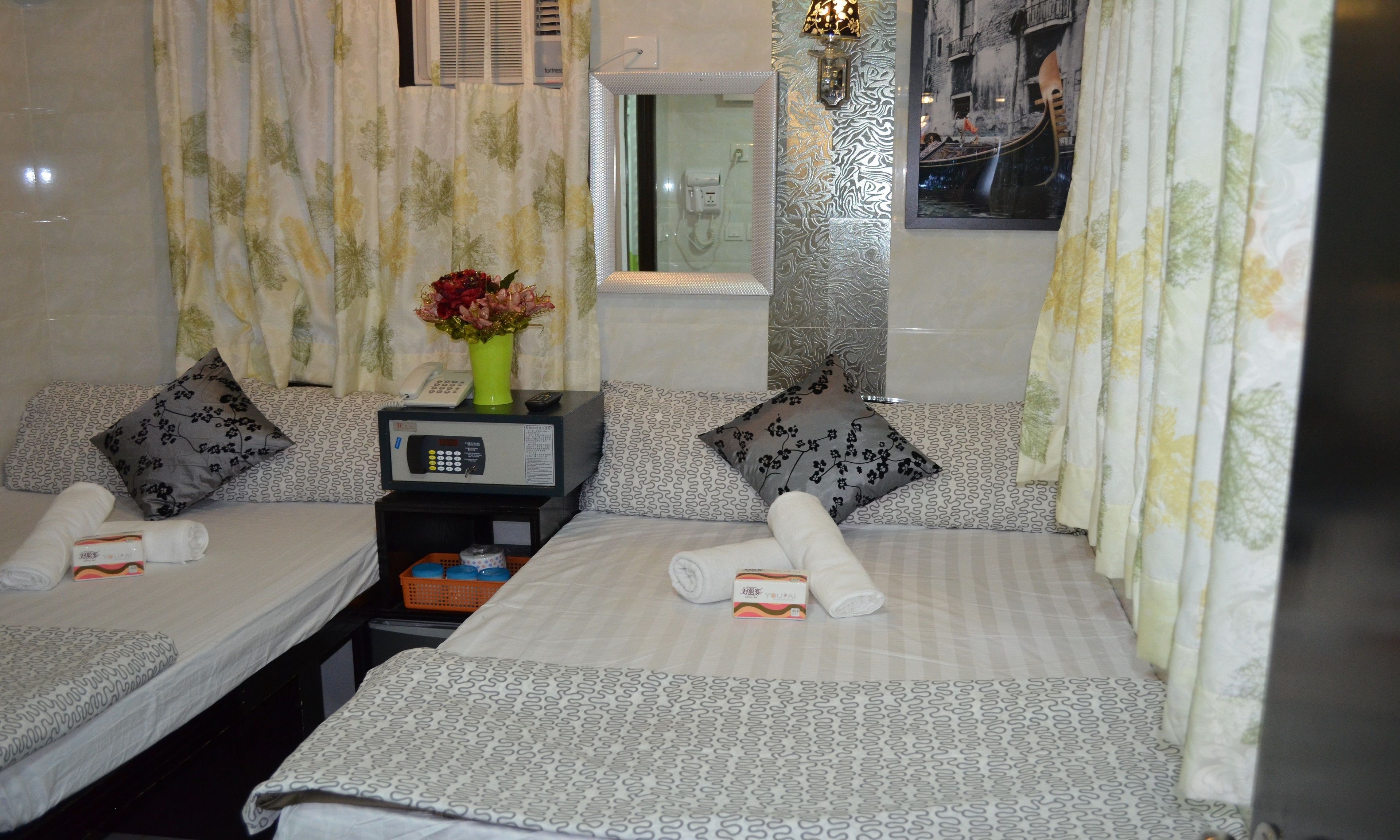 A hotel room with two beds, a bedside table with a phone and a remote control, a vase with flowers, and a window with a view of a canal.