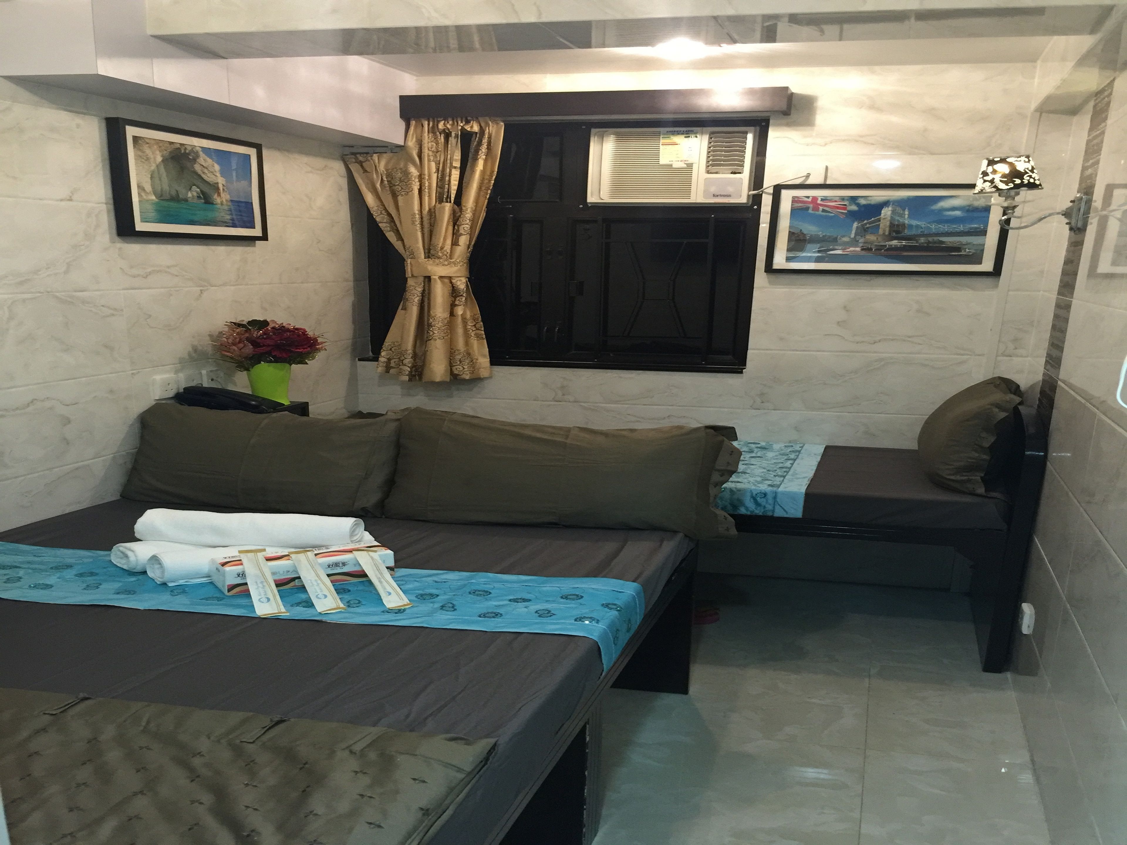 Habitación de hotel pequeña con cama, una mesita, una silla, ventana con cortinas y dos cuadros en la pared.