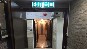 A hallway with an exit sign, a security camera, and a digital display. - Hi-Inn (Kowloon)