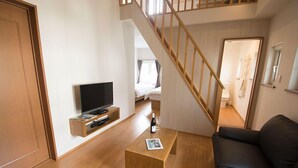 A modern living room with a wooden coffee table, a black leather sofa, a TV on a wooden shelf, and a staircase leading to another room.