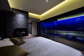 A modern bedroom with a large bed, a fireplace, and a glass wall with a night view. - Holiday Niseko Ori (Kutchan)
