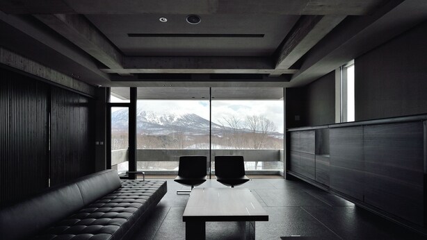 A modern interior with a sofa, a table, and chairs, large windows offering a mountain view.