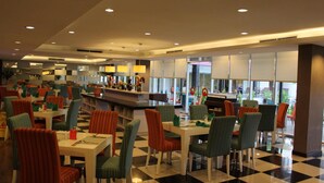 Un hall de hotel espacioso con varias zonas de restauración, un mostrador de recepción central y grandes ventanales que dejan entrar luz natural.