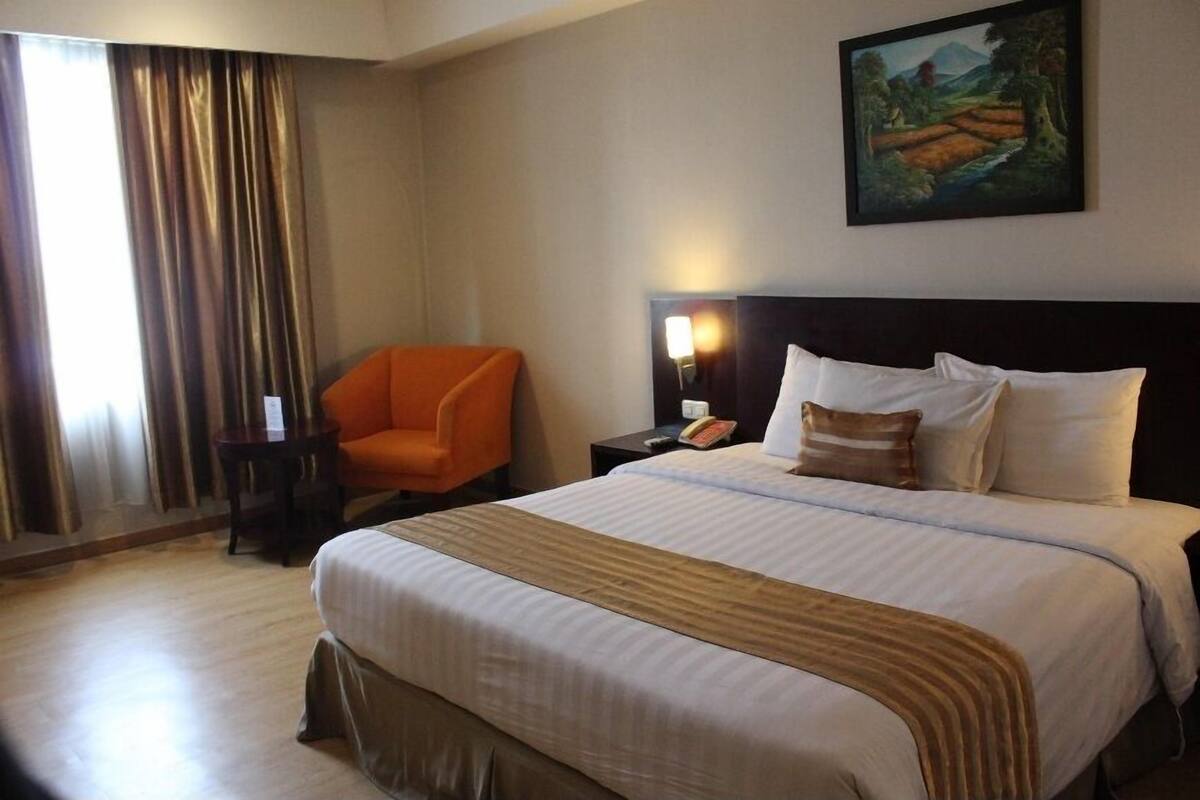 Une chambre d’hôtel avec un grand lit, une table de chevet, un fauteuil orange et un tableau au mur.