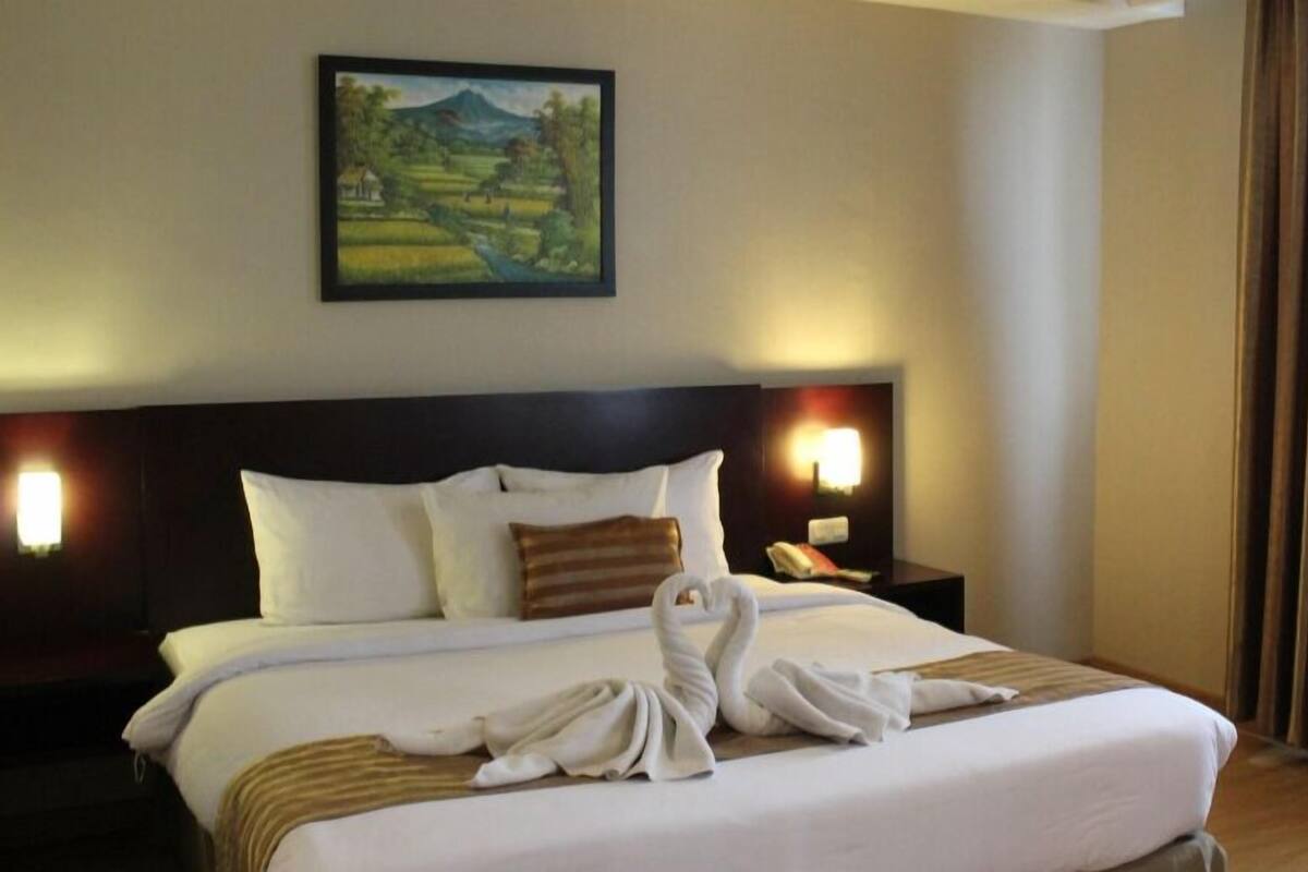 Une chambre d’hôtel avec un grand lit, deux tables de chevet, un tableau au mur et une fenêtre avec des rideaux.
