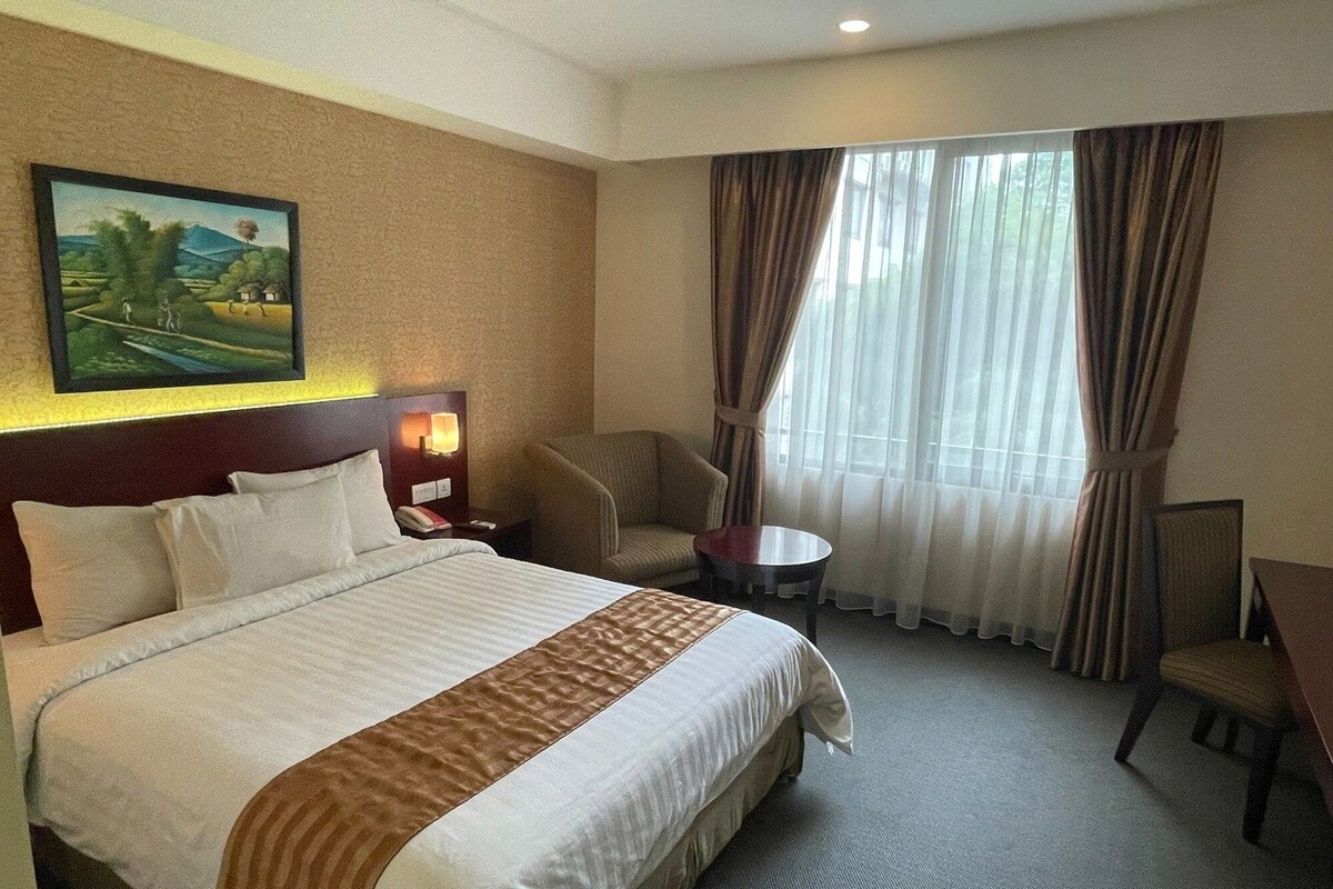 Une chambre d’hôtel avec un grand lit, un bureau, une chaise, une petite table et un tableau au mur.