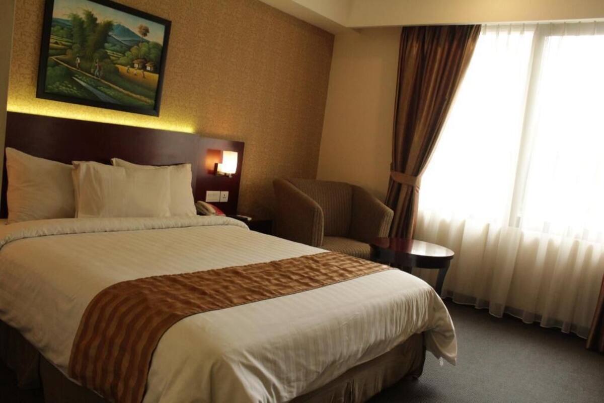 Une chambre d’hôtel avec un grand lit, une chaise, une petite table et un tableau au mur.