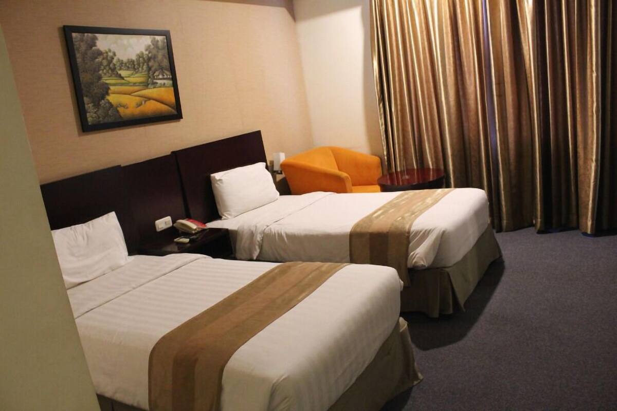 Une chambre d’hôtel avec deux lits, une table de chevet, un fauteuil orange et un tableau au mur.