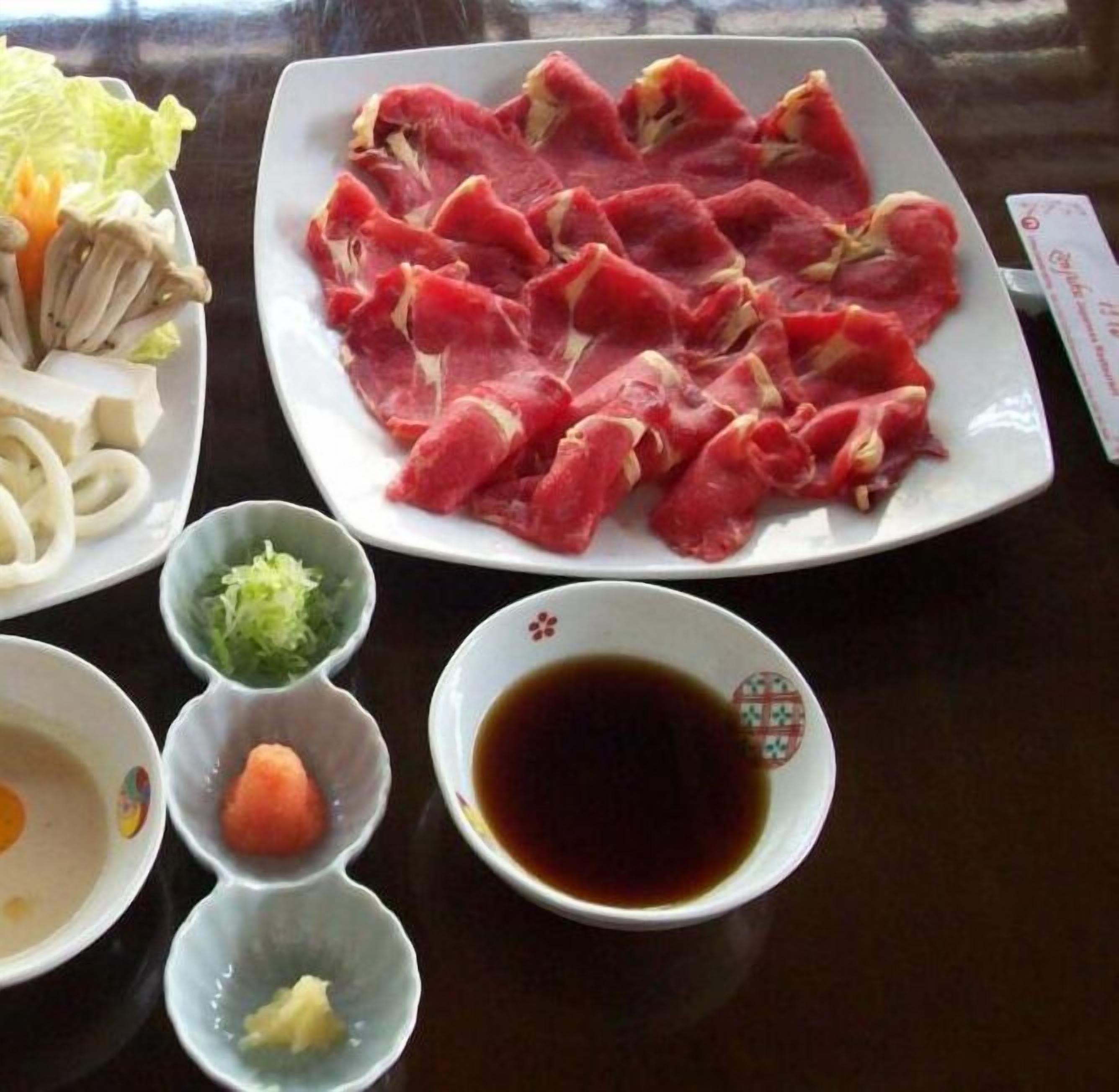 A table with various food items including raw meat, vegetables, and condiments.