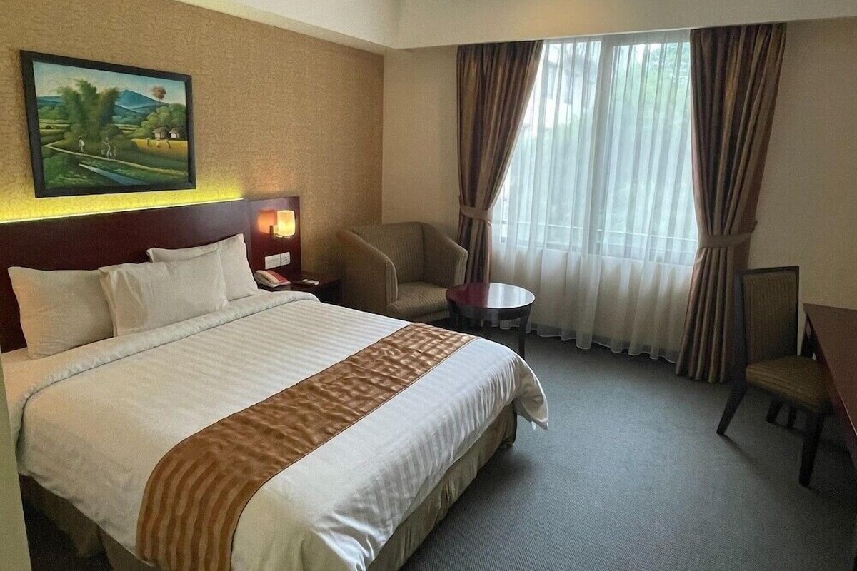 Une chambre d’hôtel avec un grand lit, une chaise, une petite table et un tableau au mur.