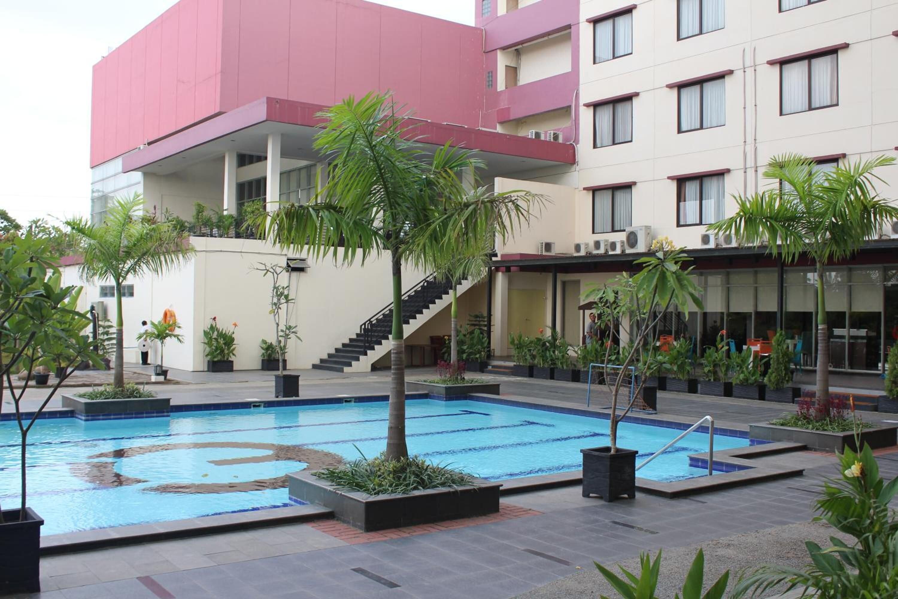 Una piscina rodeada de macetas con plantas y un edificio de varios pisos con balcones.