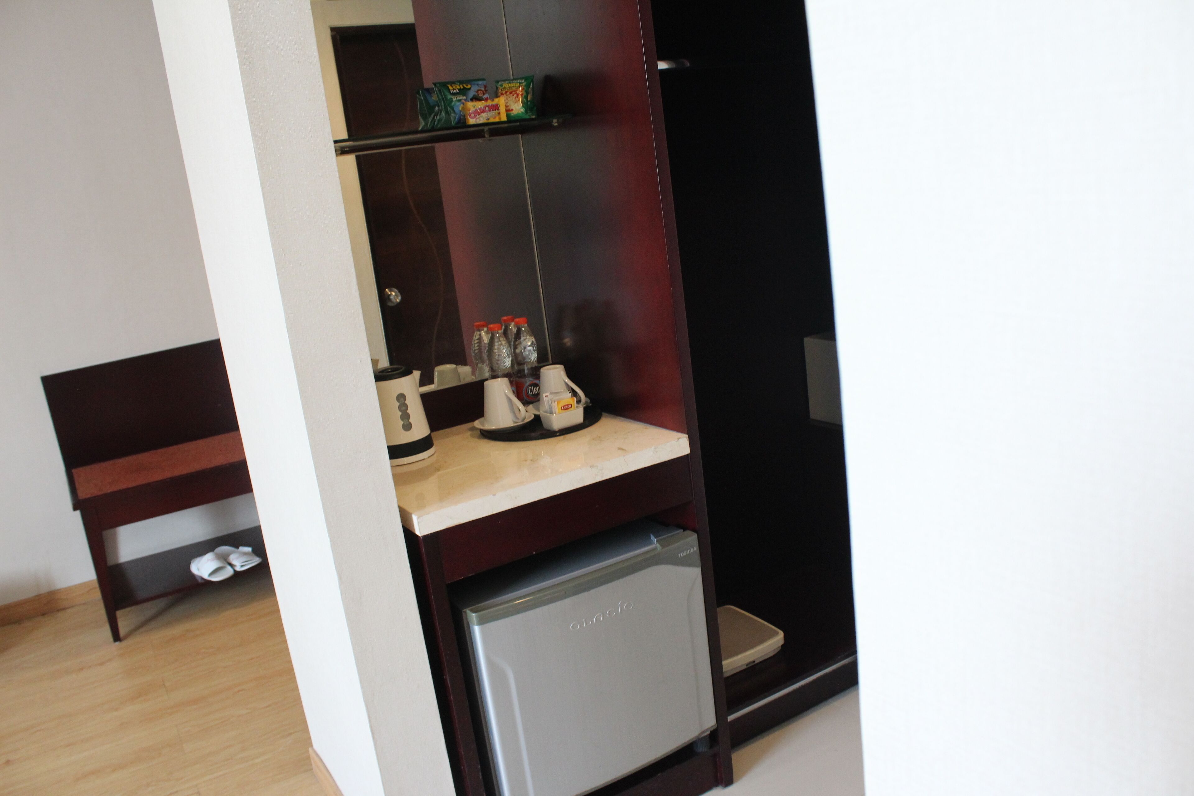A compact kitchenette with a small refrigerator, a coffee maker, and a shelf with condiments.