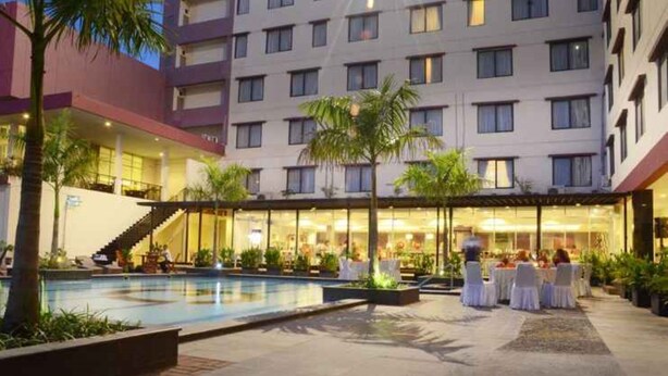 Un patio de hotel con piscina, mobiliario exterior y zona de comedor cubierta.