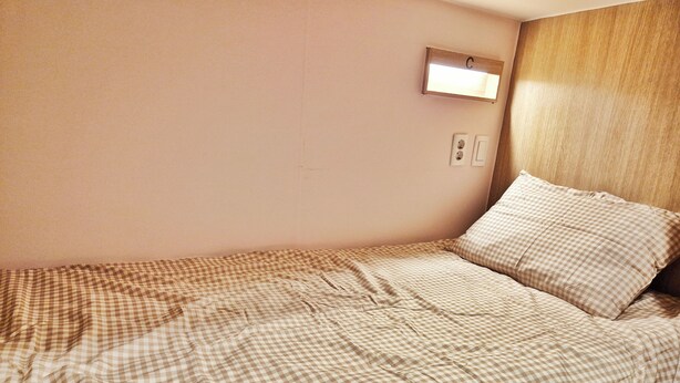 A single bed with a checkered bedspread, a bedside lamp, and a wooden headboard. - onjung stay (Busan)