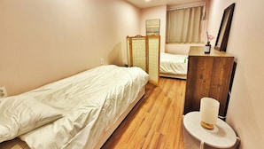 Une petite chambre à coucher, bien rangée, avec deux lits simples, une commode en bois, un miroir et une table de chevet avec une lampe.