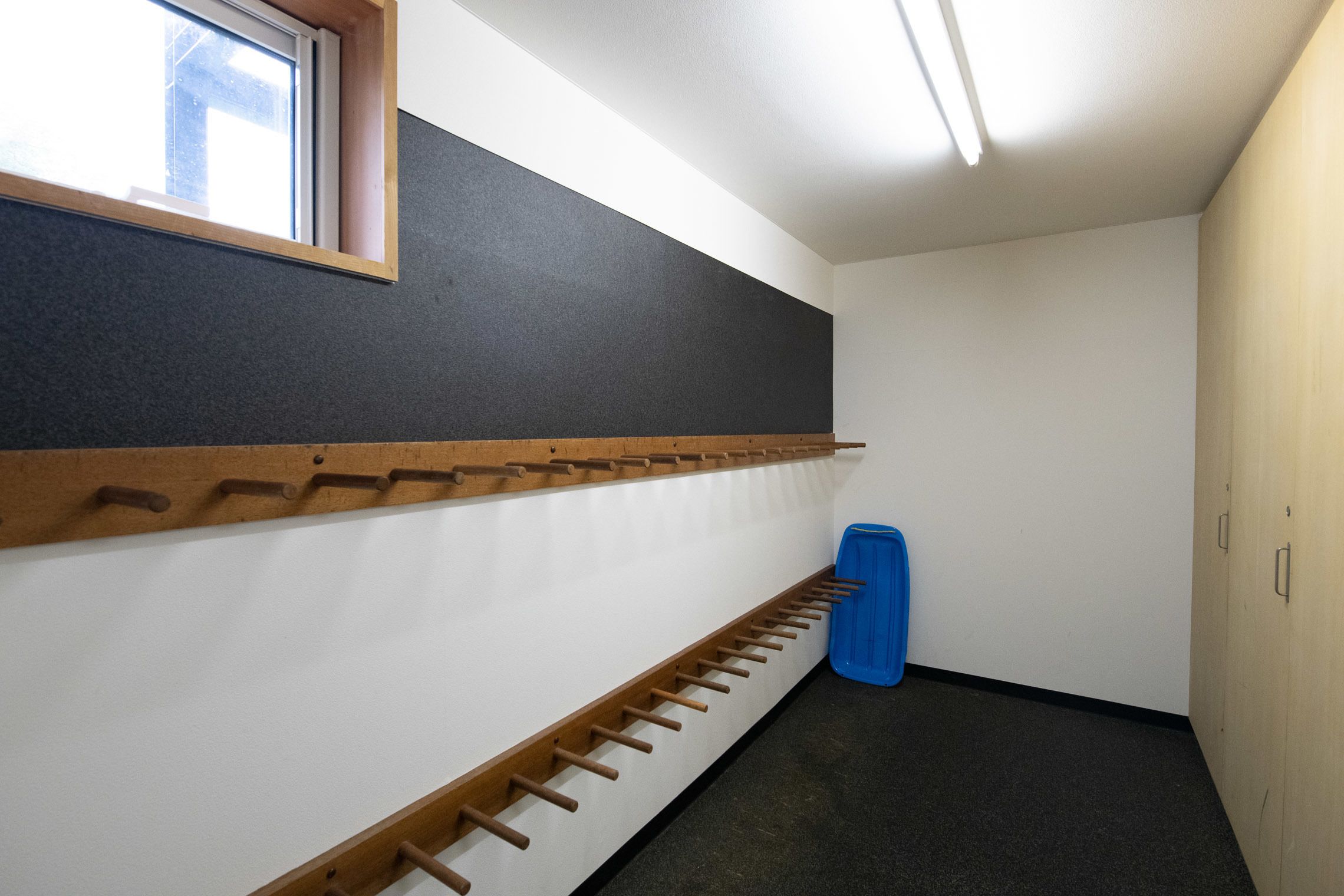 A narrow hallway with a wooden rack against the wall, a blue trash bin, and a window at the end.