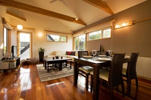 A spacious living area with a wooden floor, a sofa, a coffee table, and a dining table set for four. - Holiday Niseko Shinsetsu Apartments (Kutchan)