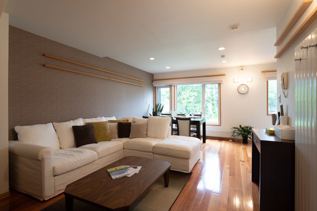 A modern living room with a sectional sofa, a coffee table, and a dining area with a table and chairs.
