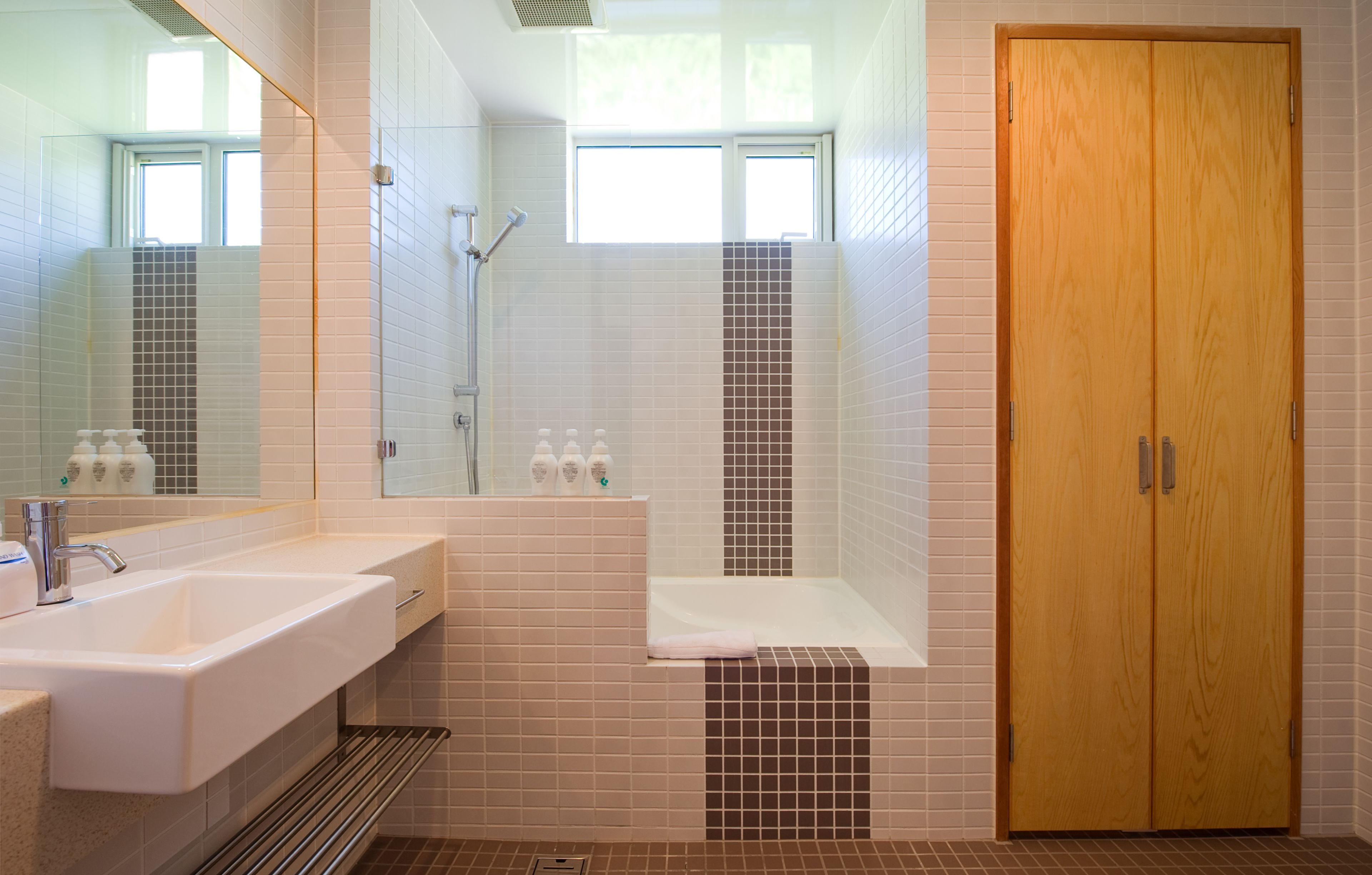 Ein Badezimmer mit einem großen Spiegel, einem Waschbecken, einer Dusche und einer Holztür.