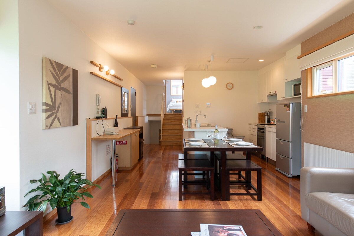 A modern kitchen with wooden flooring, a dining area with a table and chairs, and a living area with a sofa.