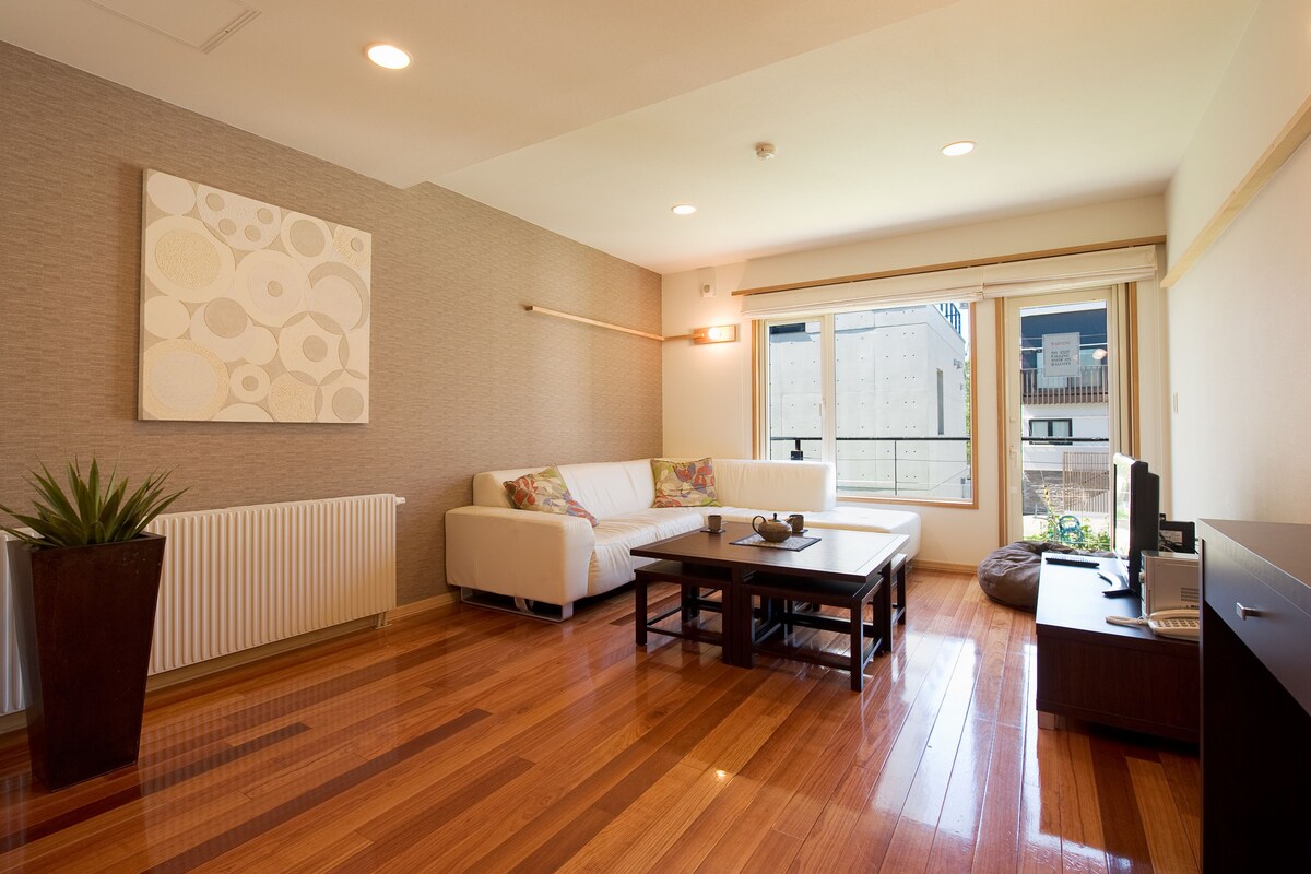 A modern living room with a white sofa, a wooden coffee table, and a large window with a view of the outside.