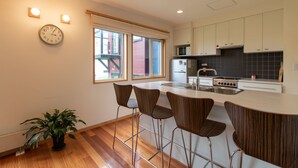 A modern kitchen with a central island, bar stools, a clock, and a potted plant. - Holiday Niseko Shinsetsu Apartments (Kutchan)