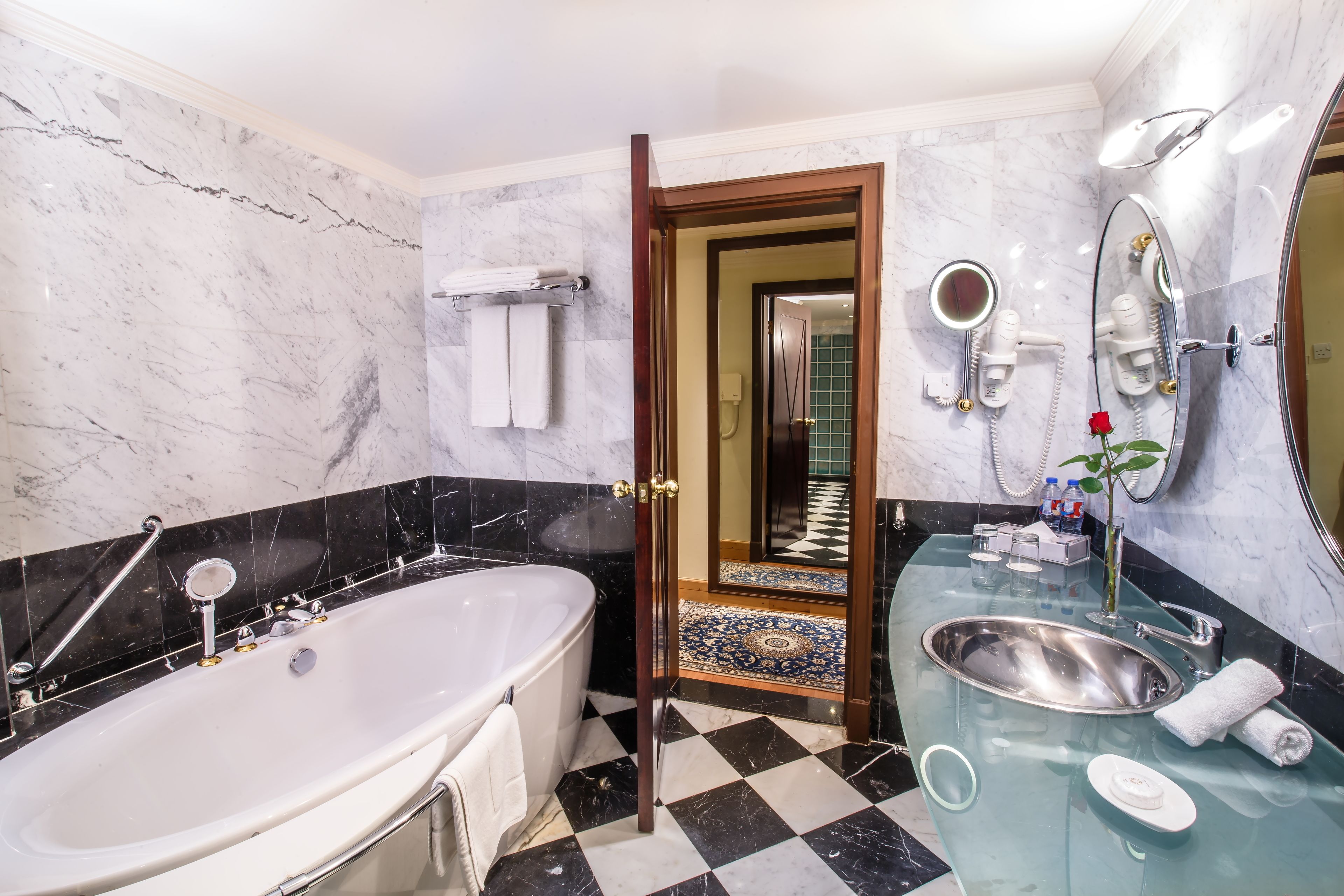 A modern bathroom with a large bathtub, a glass-enclosed sink, and a vanity mirror.