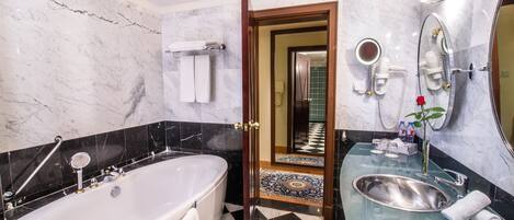 A modern bathroom with a large bathtub, a glass-enclosed sink, and a vanity mirror.