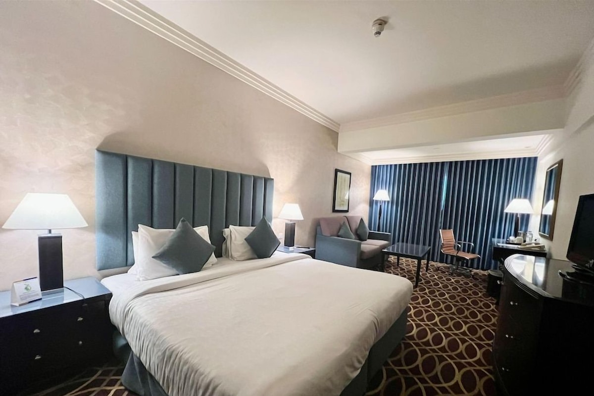 Une chambre d’hôtel avec un grand lit, deux tables de chevet, un bureau, une chaise et un téléviseur.
