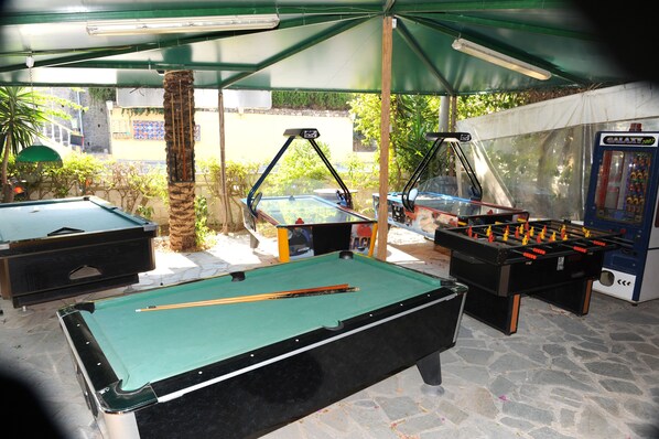A pool table, foosball table, and a foosball machine in an outdoor covered area.