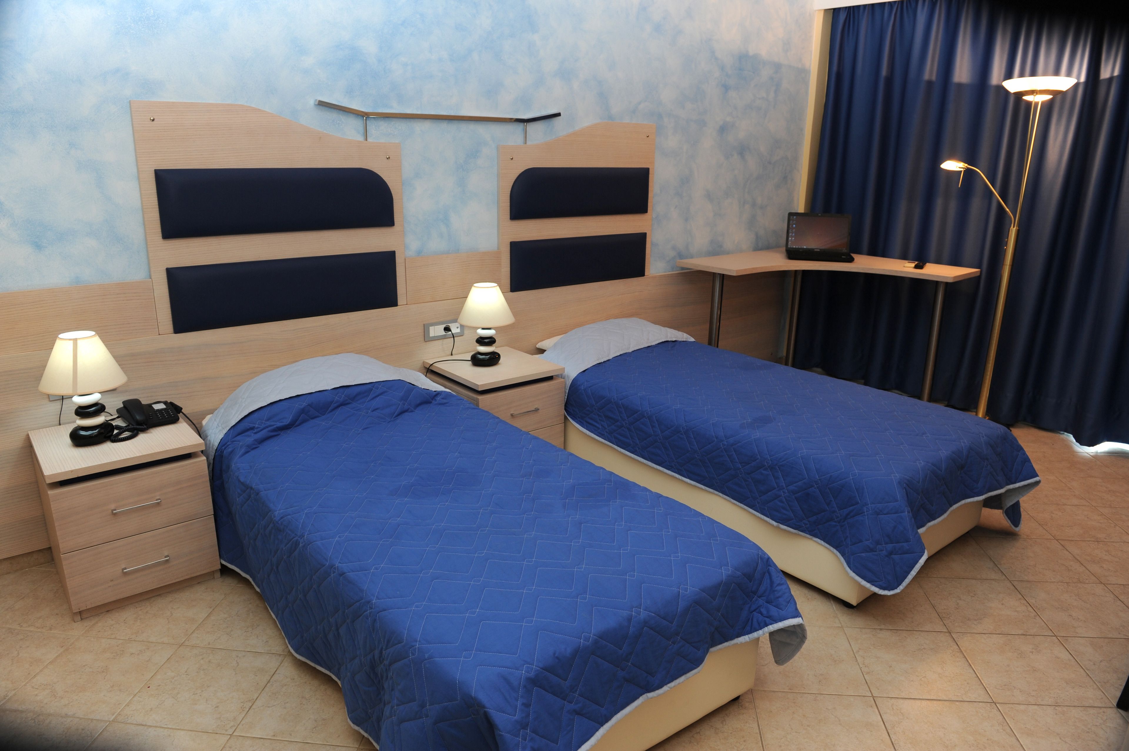 A hotel room with two single beds, a desk, a chair, a lamp, and a telephone.