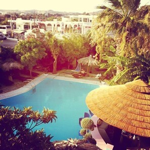A swimming pool surrounded by tropical plants and a thatched-roof structure.