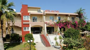 Un hotel con fachada roja y color beige, un balcón con macetas y una escalera que conduce a la entrada.