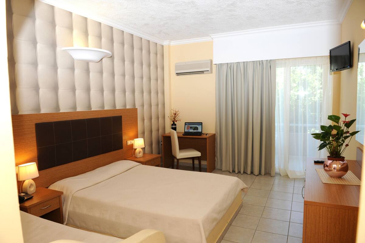 A hotel room with a large bed, a desk with a computer, a TV, and a potted plant.