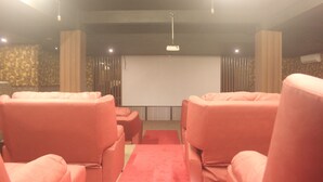 A room with a large screen, red upholstered chairs, and a red carpet. - The L Hotel Entertainment (Batam)