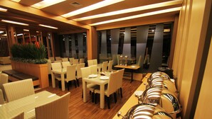 A restaurant with a long dining table, multiple chairs, and a buffet line with food containers. - The L Hotel Entertainment (Batam)