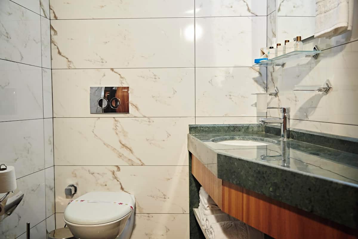 A bathroom with a marble tile wall, a toilet, a sink with a wooden vanity, and a mirror with a glass shelf above it.