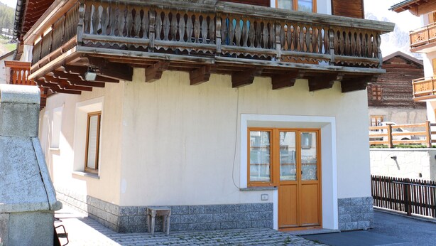 Un chalet en bois doté d’un balcon, d’un escalier en pierre et d’une cour pavée.