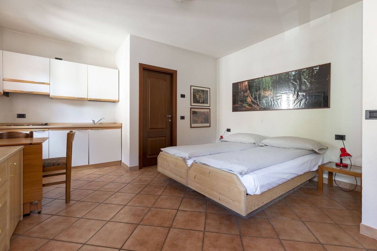 A bedroom with a bed, a desk, and a chair. There is a door leading to another room.