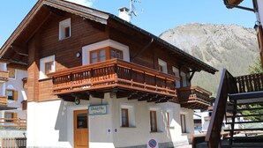 Un chalet en bois doté d’un balcon, une enseigne indiquant « Chalet Oltia » et un panneau indiquant un espace de stationnement privé.
