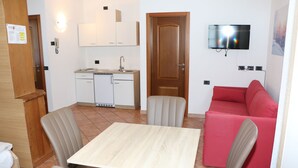 Un espace de vie compact comprenant une table à manger, des chaises, un coin cuisine, un canapé rouge et un téléviseur fixé au mur.
