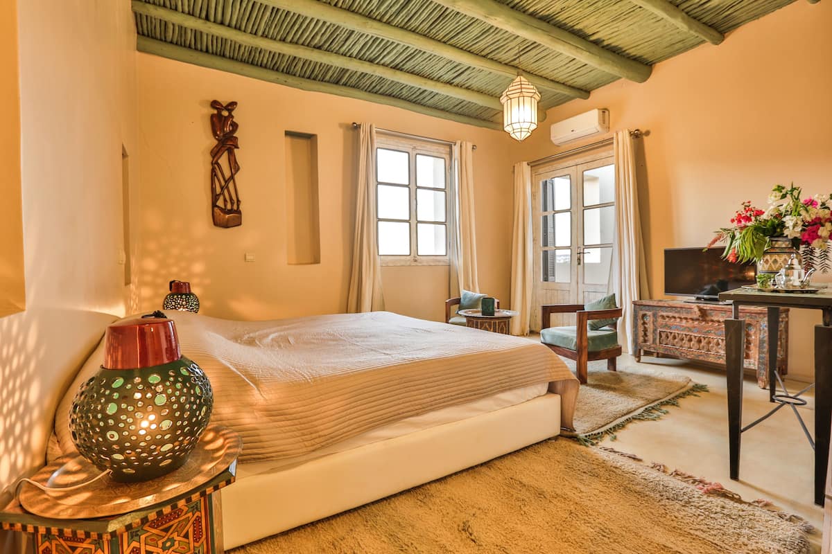 A cozy bedroom with a bed, a decorative vase, a small table, and a desk with a vase of flowers.