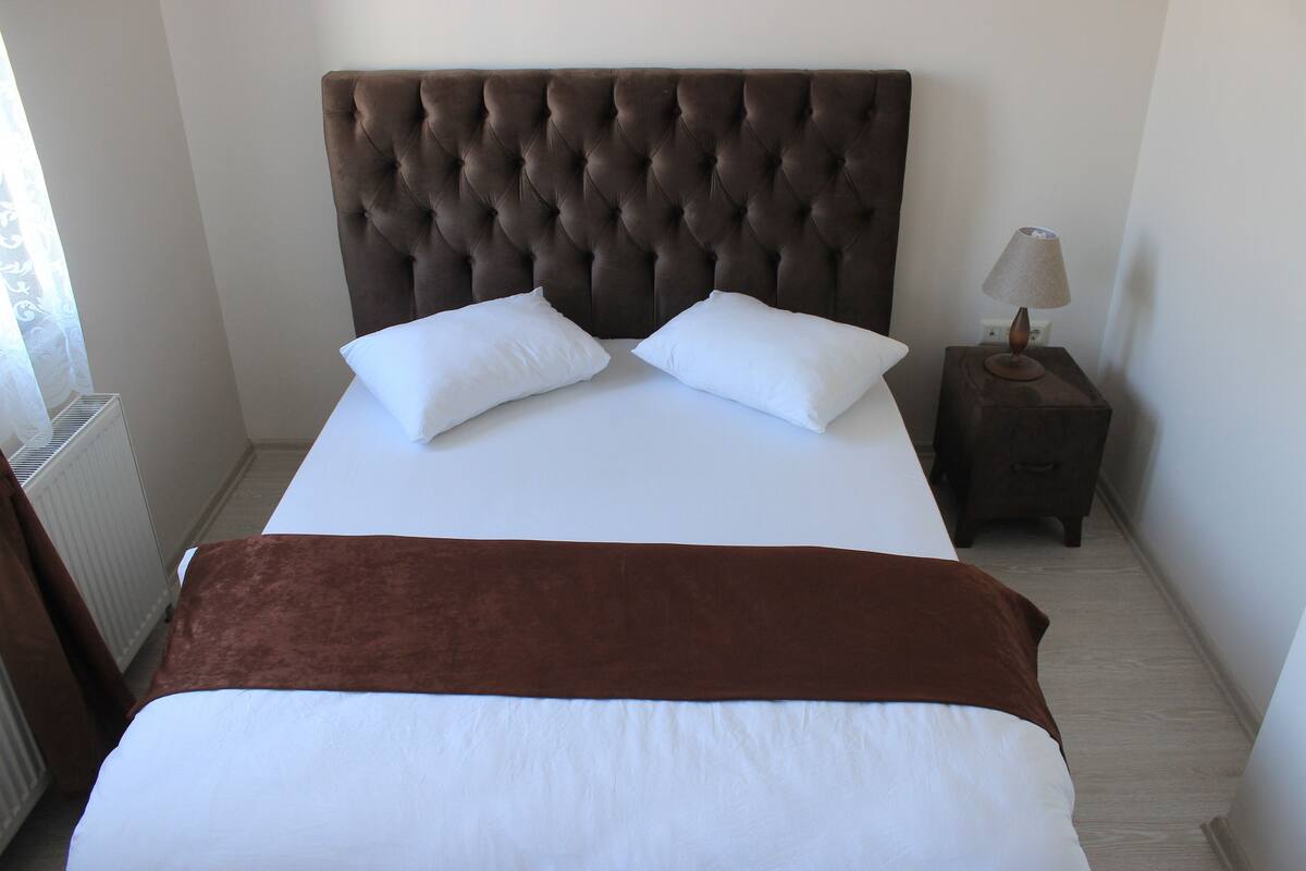 A neatly made bed with a brown headboard, white pillows, and a brown throw blanket.